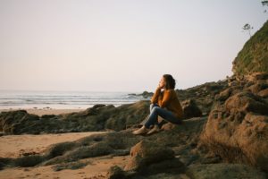 Photo of a woman sitting on rocks on the beach. This represents how therapy for anxiety in San Francisco, CA can help you manage your anxiety symptoms to stay calm. Learn more here!