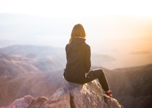 Photo of a woman sitting on a rock on a cliff. Anxiety symptoms can be overwhelming. Learn how therapy for anxiety in California can help manage anxiety symptoms.