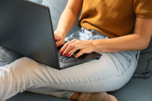 Photo of a woman sitting on a couch using a laptop. This photo represents how online therapy in California can help you manage your anxiety symptoms from the comfort of your home. Click here to learn more!