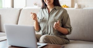Photo of a woman sitting on her couch using her laptop happily talking. This photo represents how online couples therapy in California can help you reconnect with your partner. Click here to learn more!