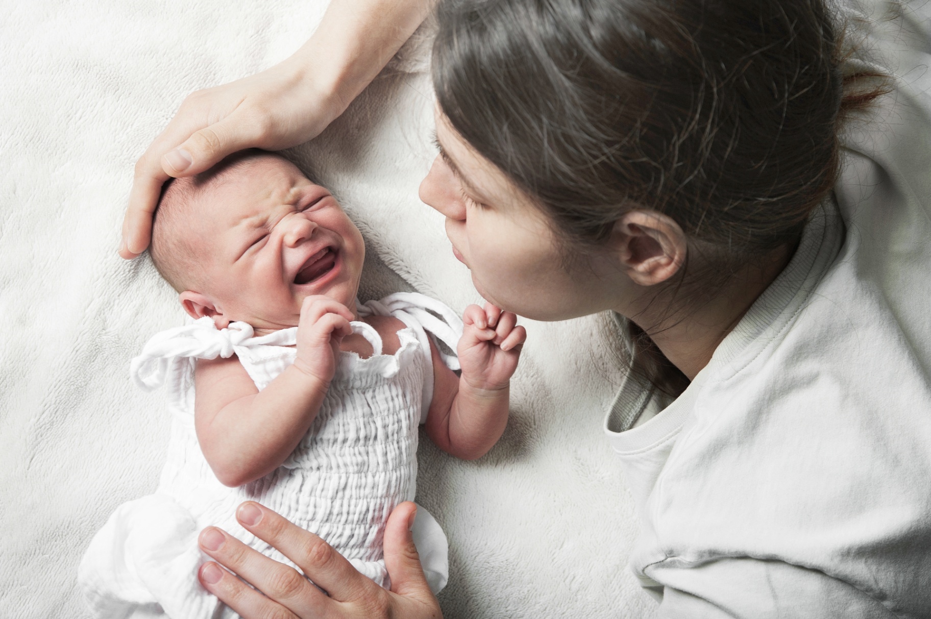 Photo of a young mom laying down comforting her baby while it cries. Suffering from postpartum anxiety? Learn how postpartum counseling in San Francisco, CA can help you heal from your postpartum symptoms.