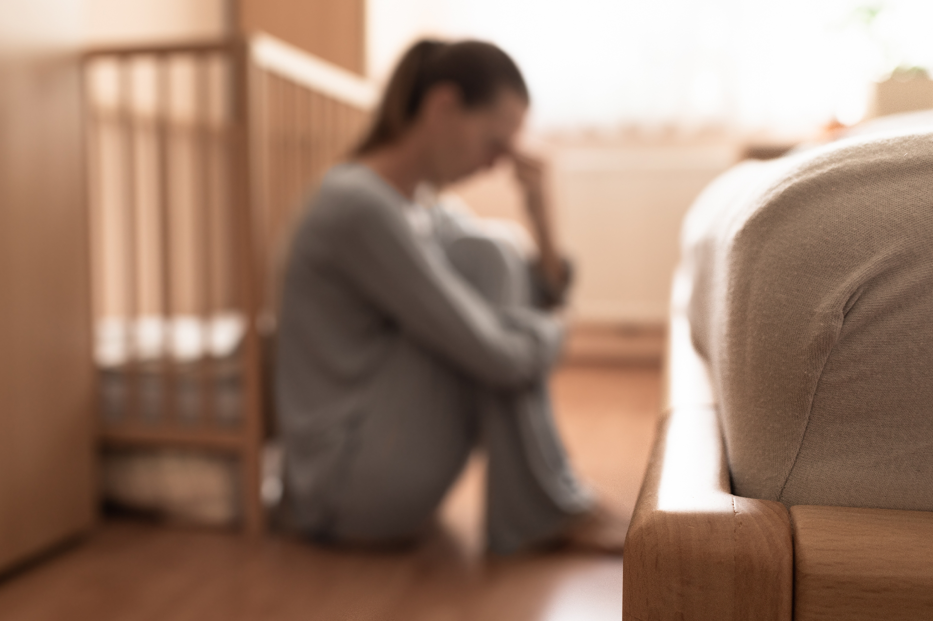 Photo of a woman sitting on the floor against a crib looking upset. This photo represents the struggles you may face after having a baby. Learn how postpartum counseling in the Bay Area, CA can help you begin to heal.
