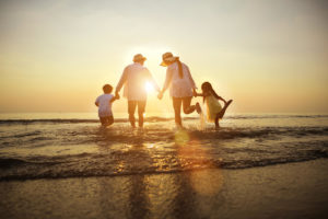Photo of a family walking into the ocean holding hands during sunset. Parent coaching in San Francisco, CA can help you become a better parent. Learn how to effectively parent here.
