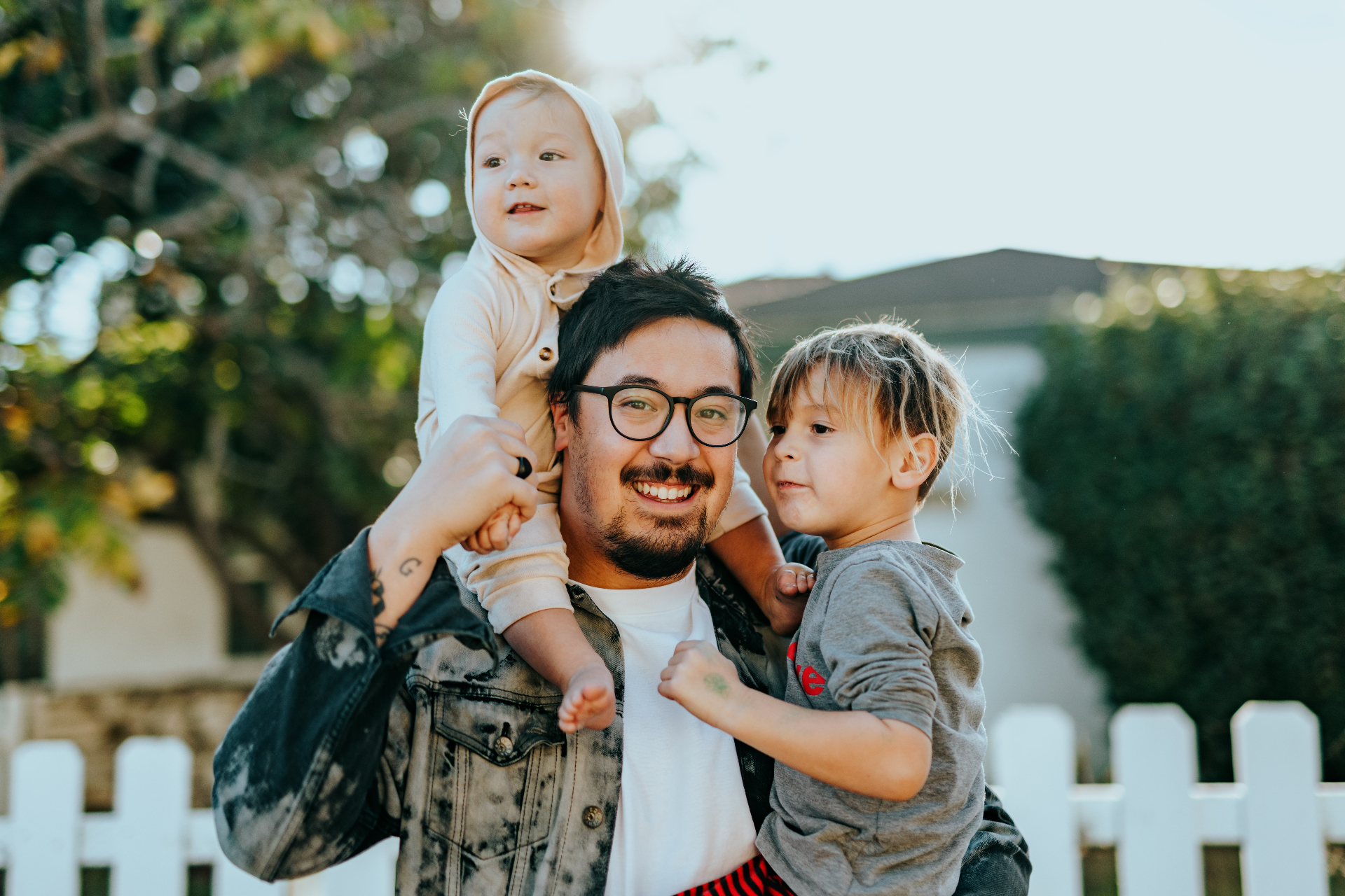 Photo of a father holding his two children outside and smiling. This photo represents how parent coaching in Marin County, CA can help you navigate your parenting style.