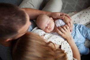 Photo of a mother and father leaning their heads together looking down holding their baby. As a new mother you may face new emotional challenges. With counseling for mothers in San Francisco, CA you can begin to manage your symtpoms.