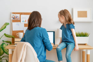 Photo of a mother sitting at a desk working on a laptop with her daughter watching her. With counseling for mothers in San Francisco, CA you can begin managing your symptoms that come with the emotional challenges of being a mother.